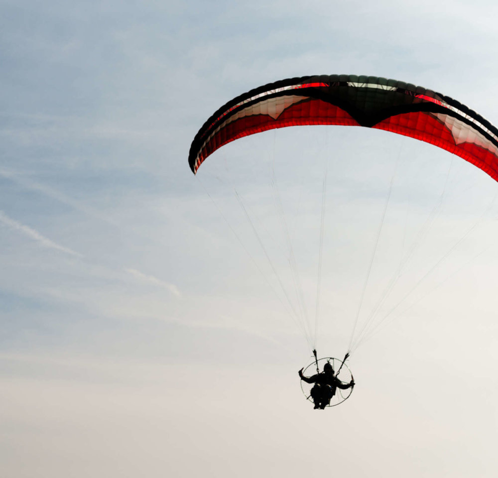 Person holds two directional controls flying with a propeller and motor below a cloth parachute